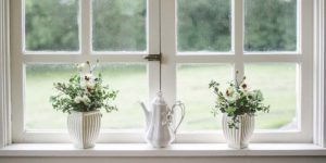 window cill with 2 white flower vases with green and white flowers in them and a white teapot