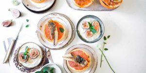 a feast of fish, figs and grapefruit set on a white table with flowers loosley placed